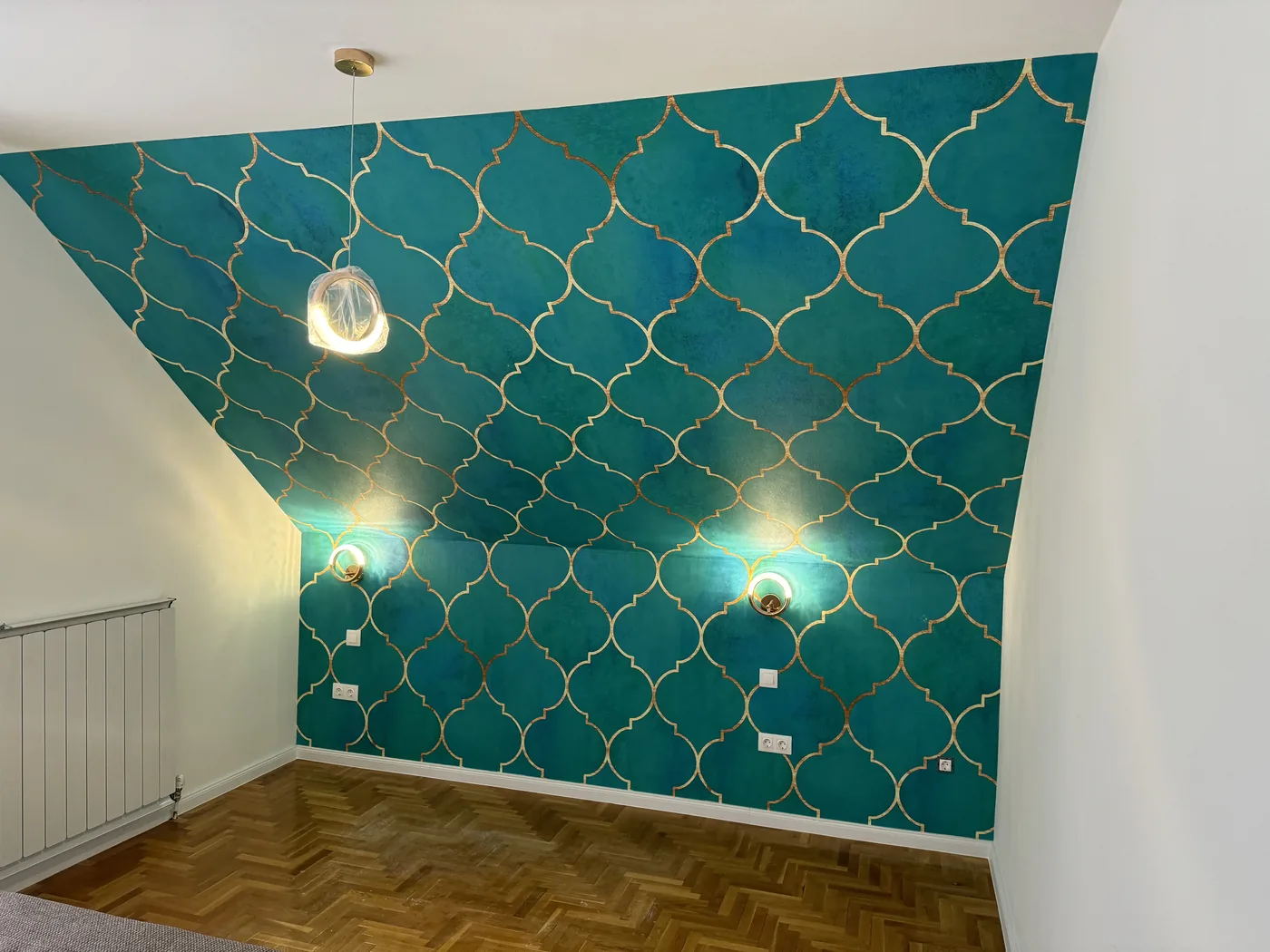 Loft room with teal wall paint and gold-patterned decorative painting, herringbone parquet, pendant and wall lights.